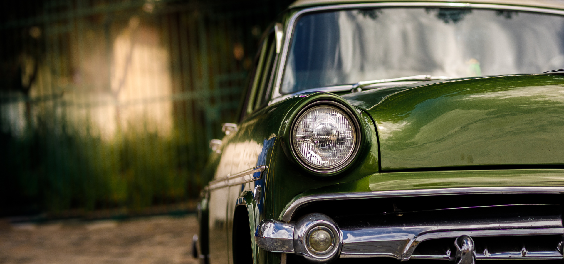 Close-up of a vintage green car’s front end with a chrome bumper and round headlight