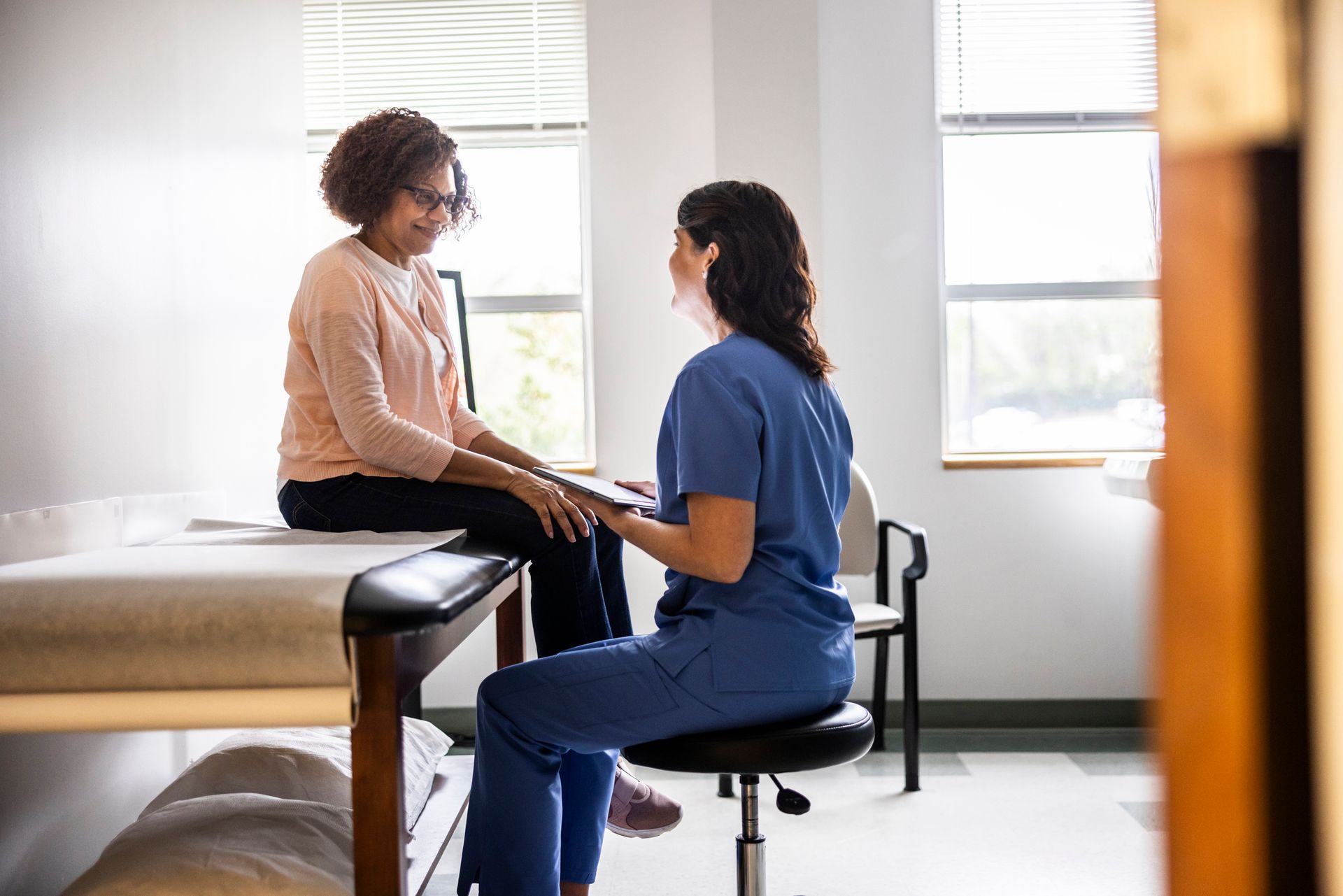 A nurse is sitting on a stool talking to a patient.