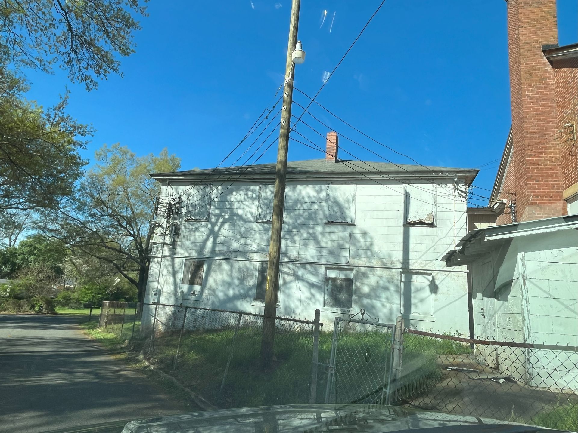 A white house with a brick chimney is behind a chain link fence