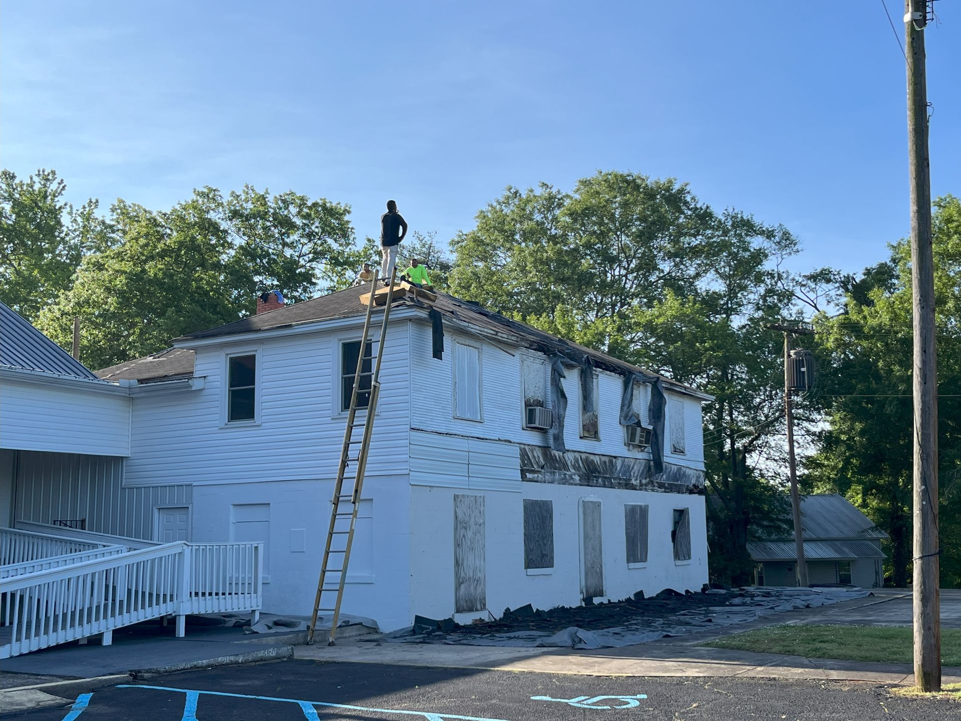 A man is standing on a ladder on the roof of a white building.