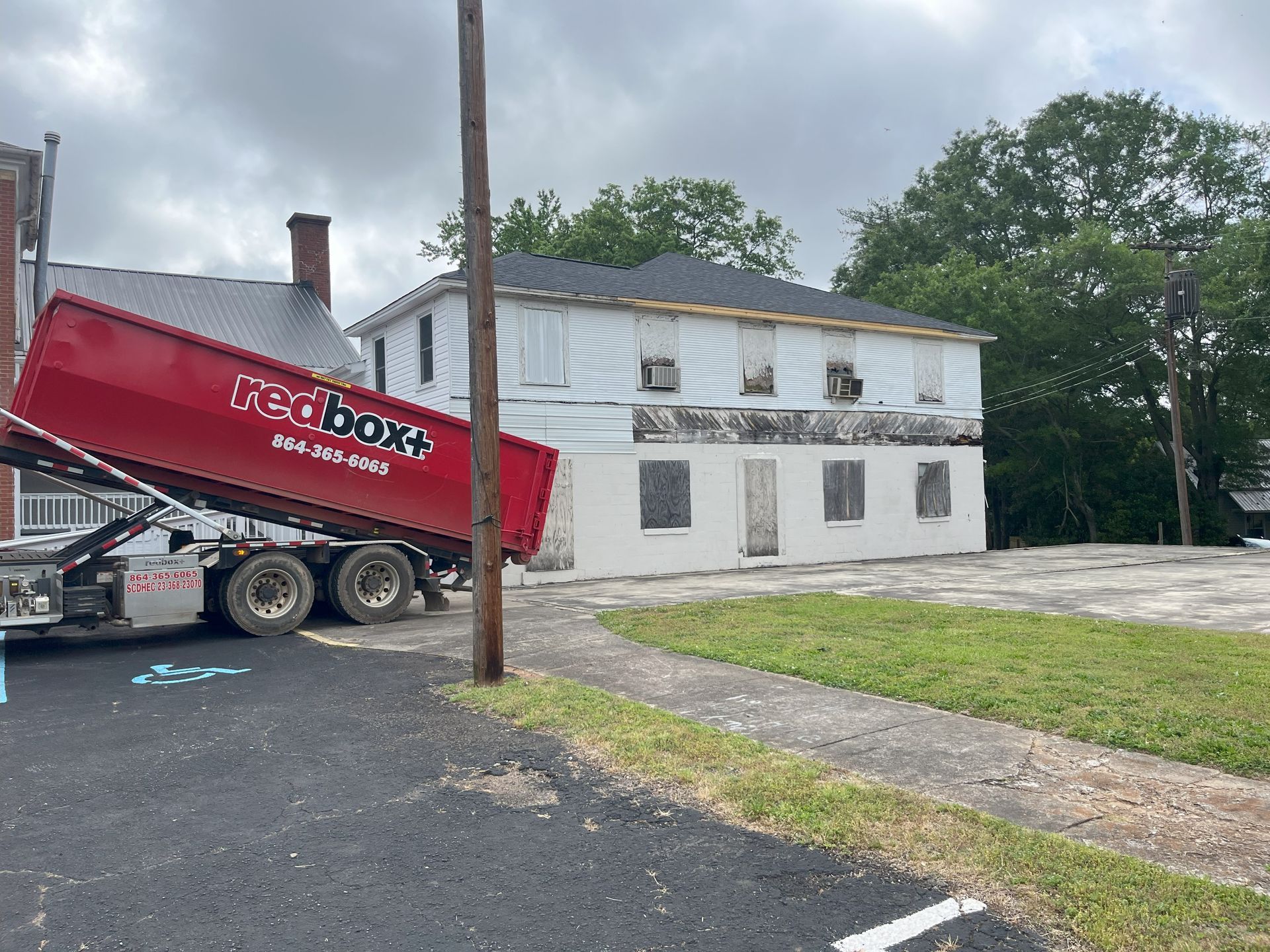 A red dumpster is sitting in front of a white house.
