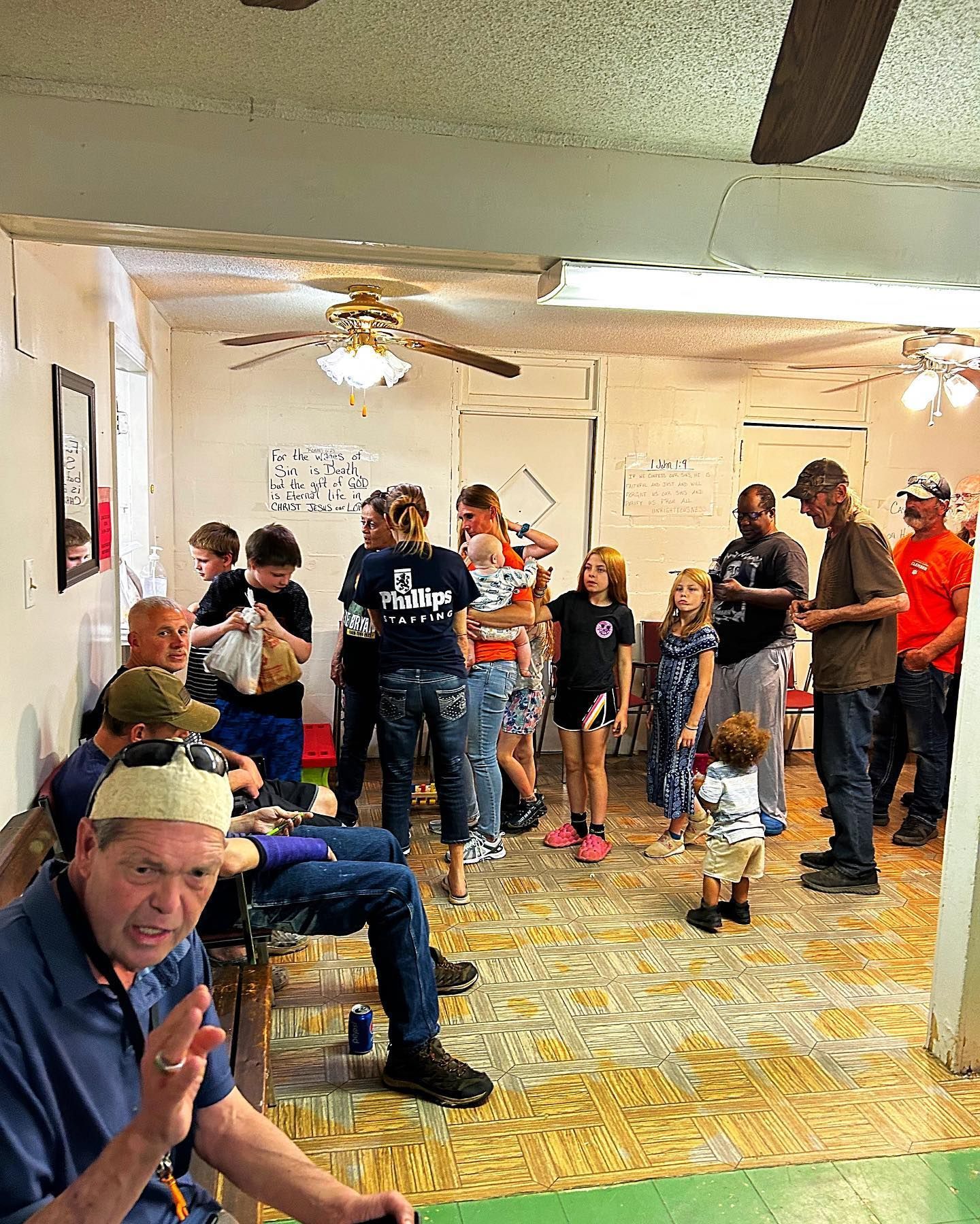 A group of people are gathered in a room with a ceiling fan.