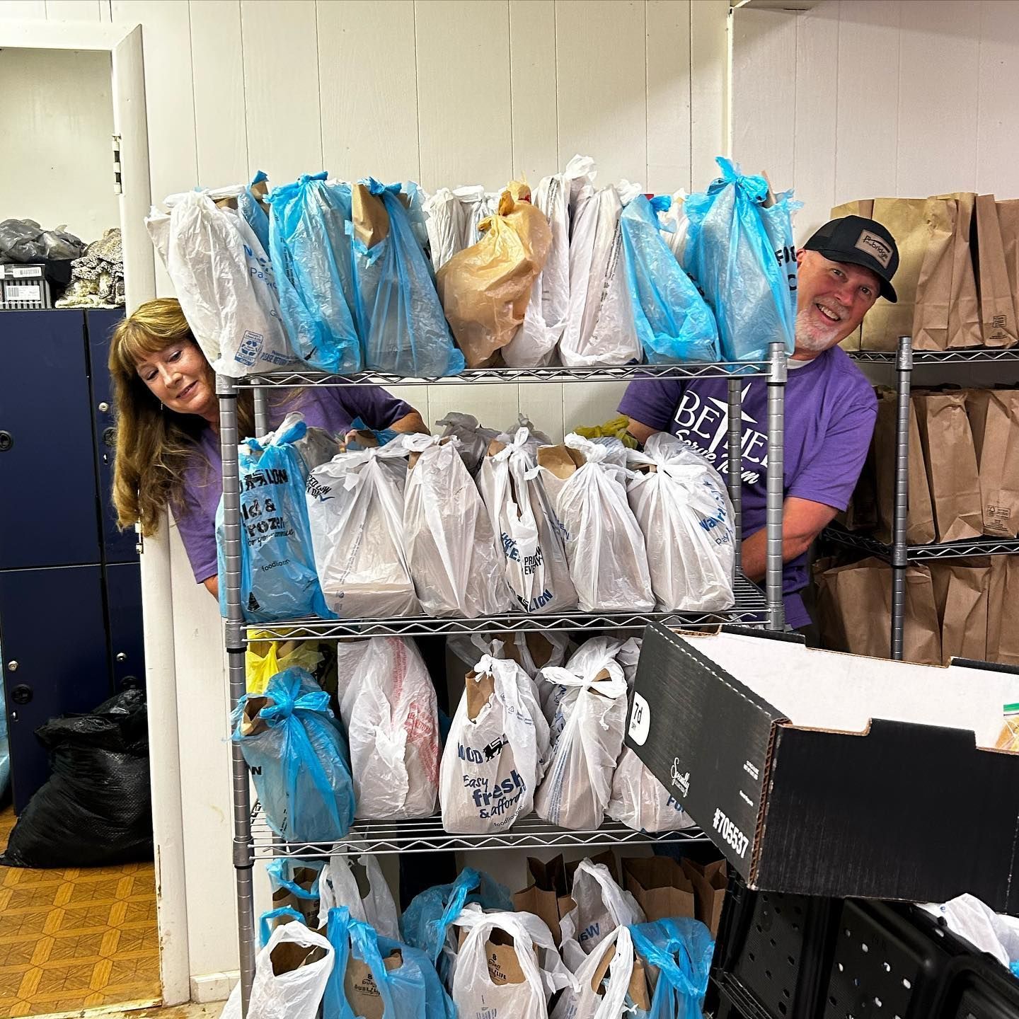 A man and a woman are standing in front of a shelf full of bags.