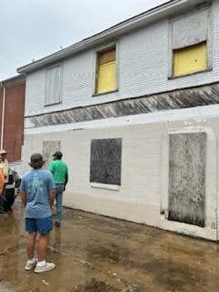 A group of people are standing in front of a white building with yellow windows.