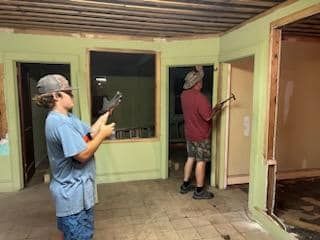 Two men are standing in a room holding hammers.