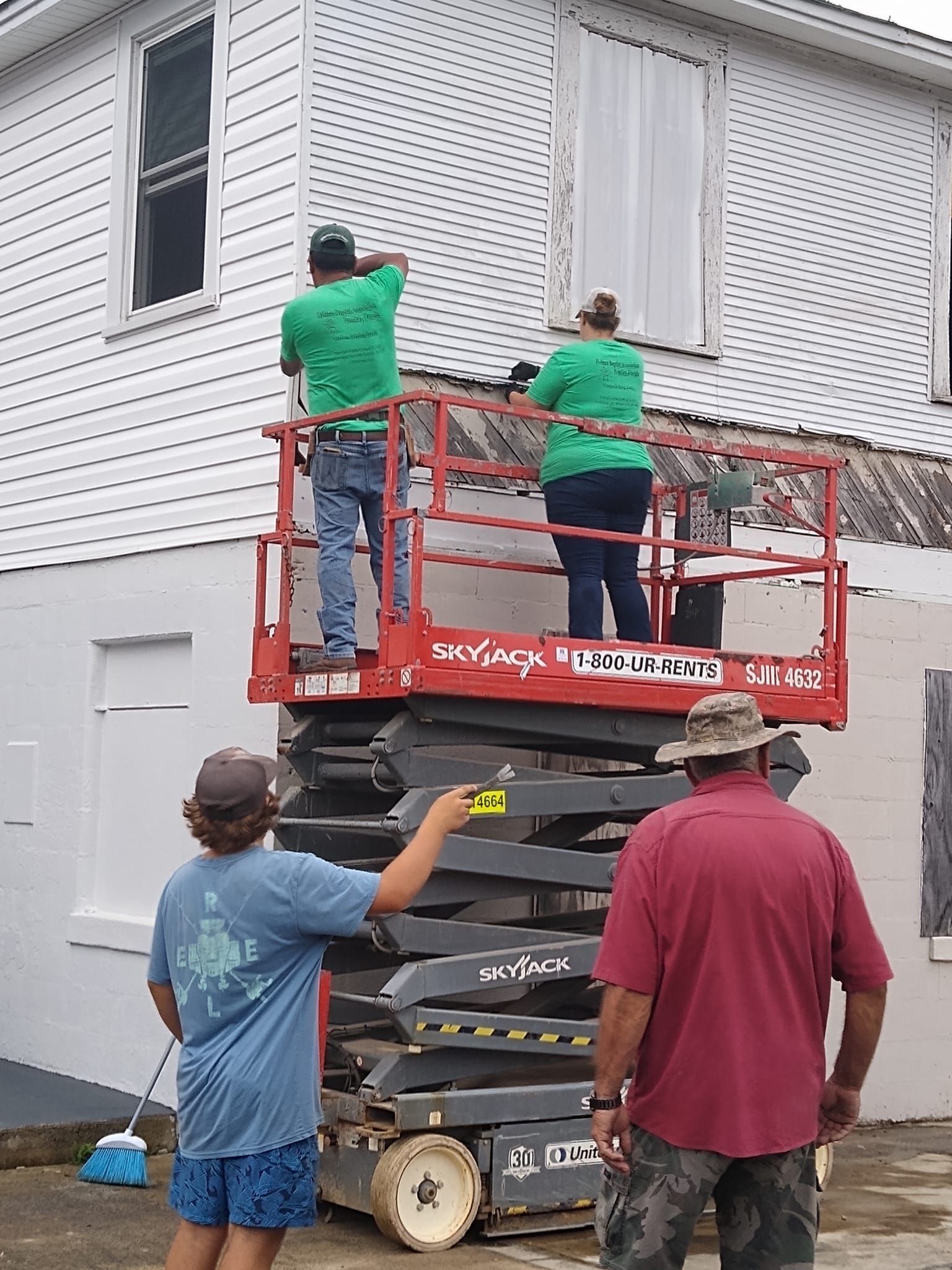 A group of people are working on a house with a scissor lift.