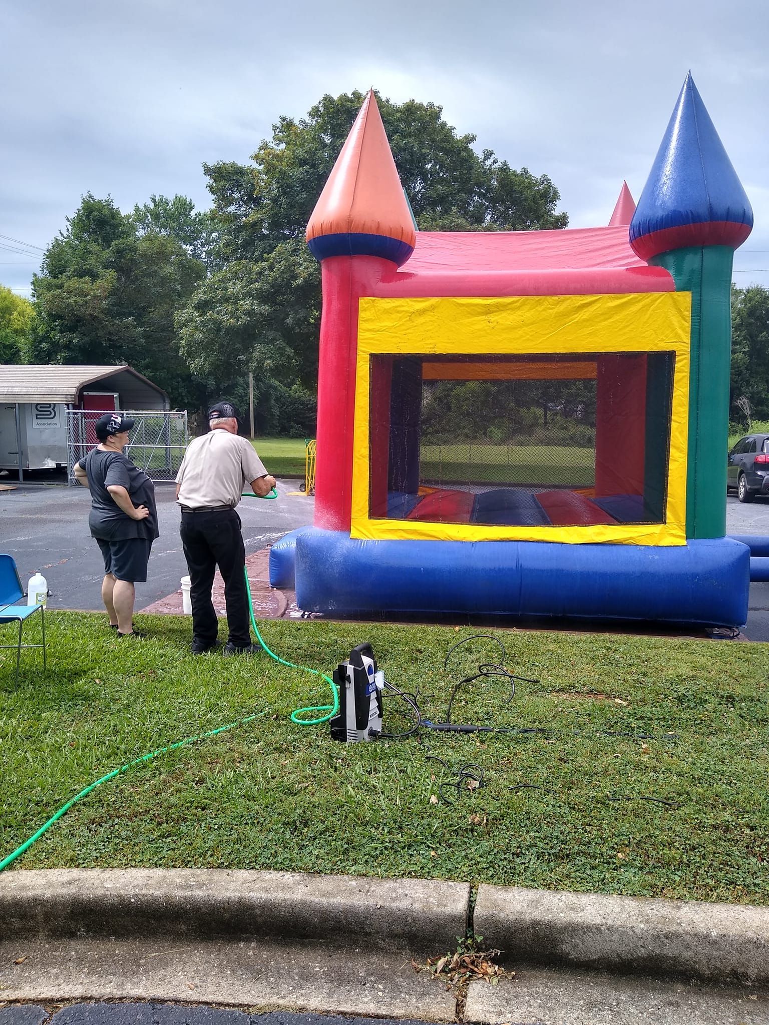 A man is standing next to a colorful bouncy house in a parking lot.
