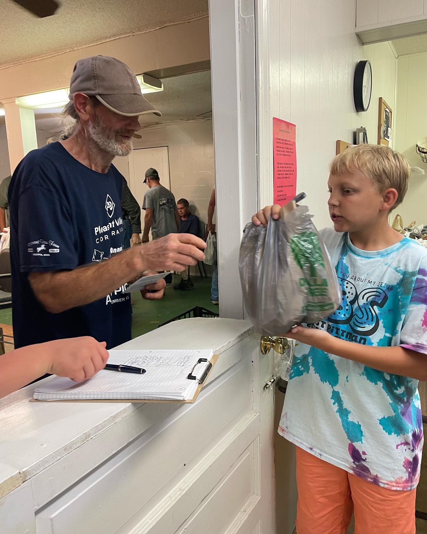 A man and a boy are standing in front of a counter . the boy is holding a bag of food.