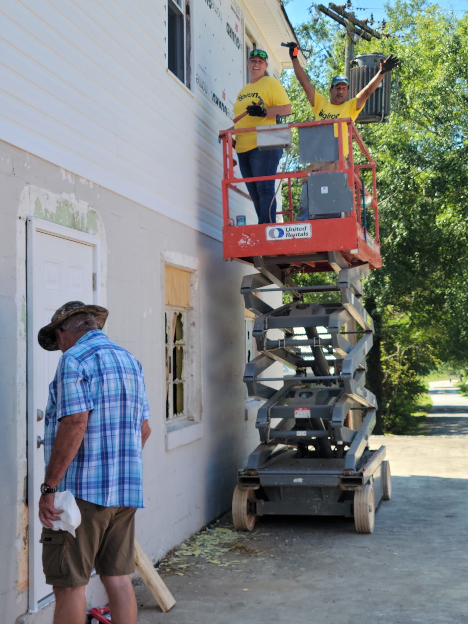 A man in a plaid shirt is standing next to a man on a scissor lift.