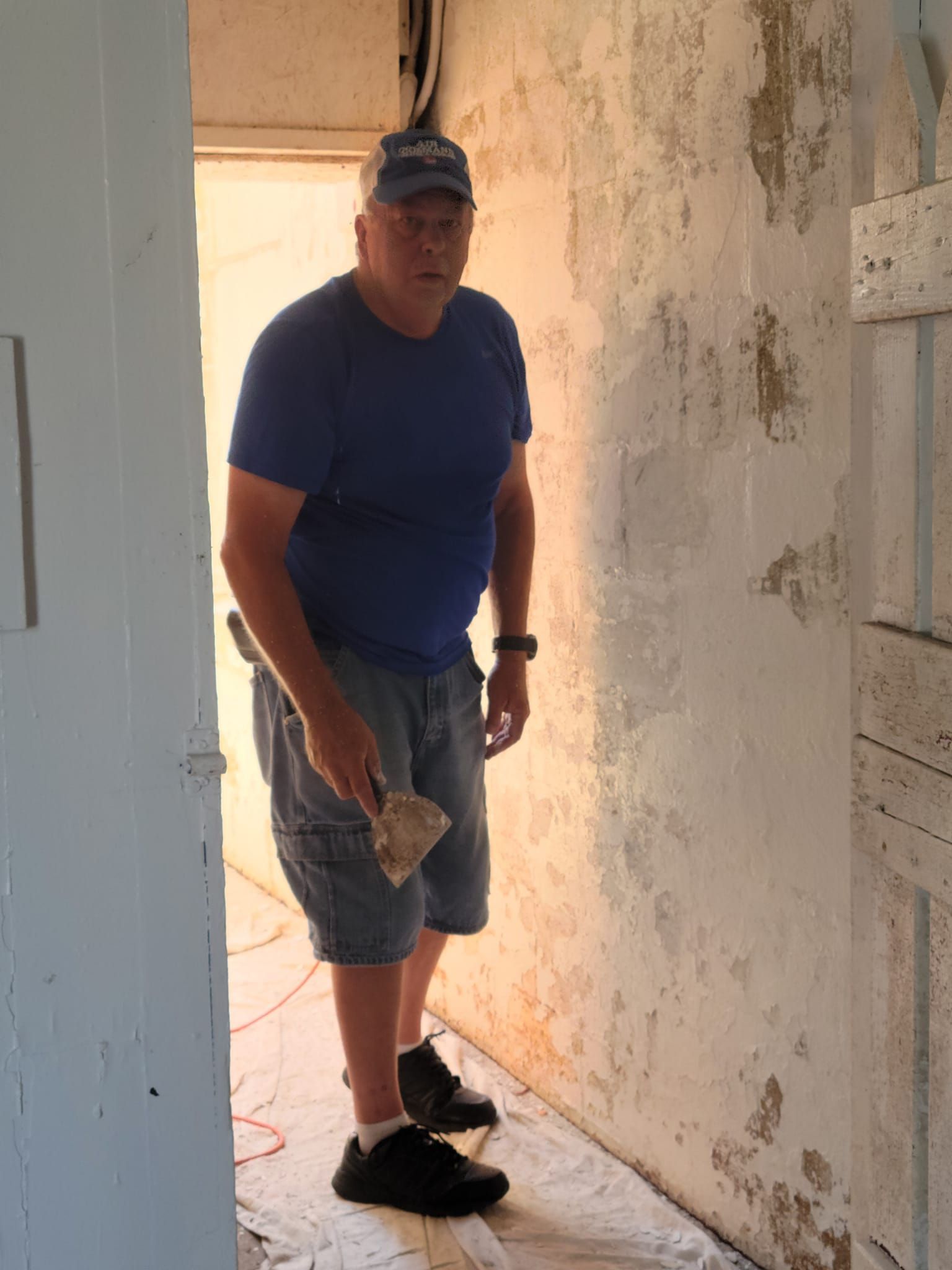 A man in a blue shirt is standing in a hallway holding a spatula.