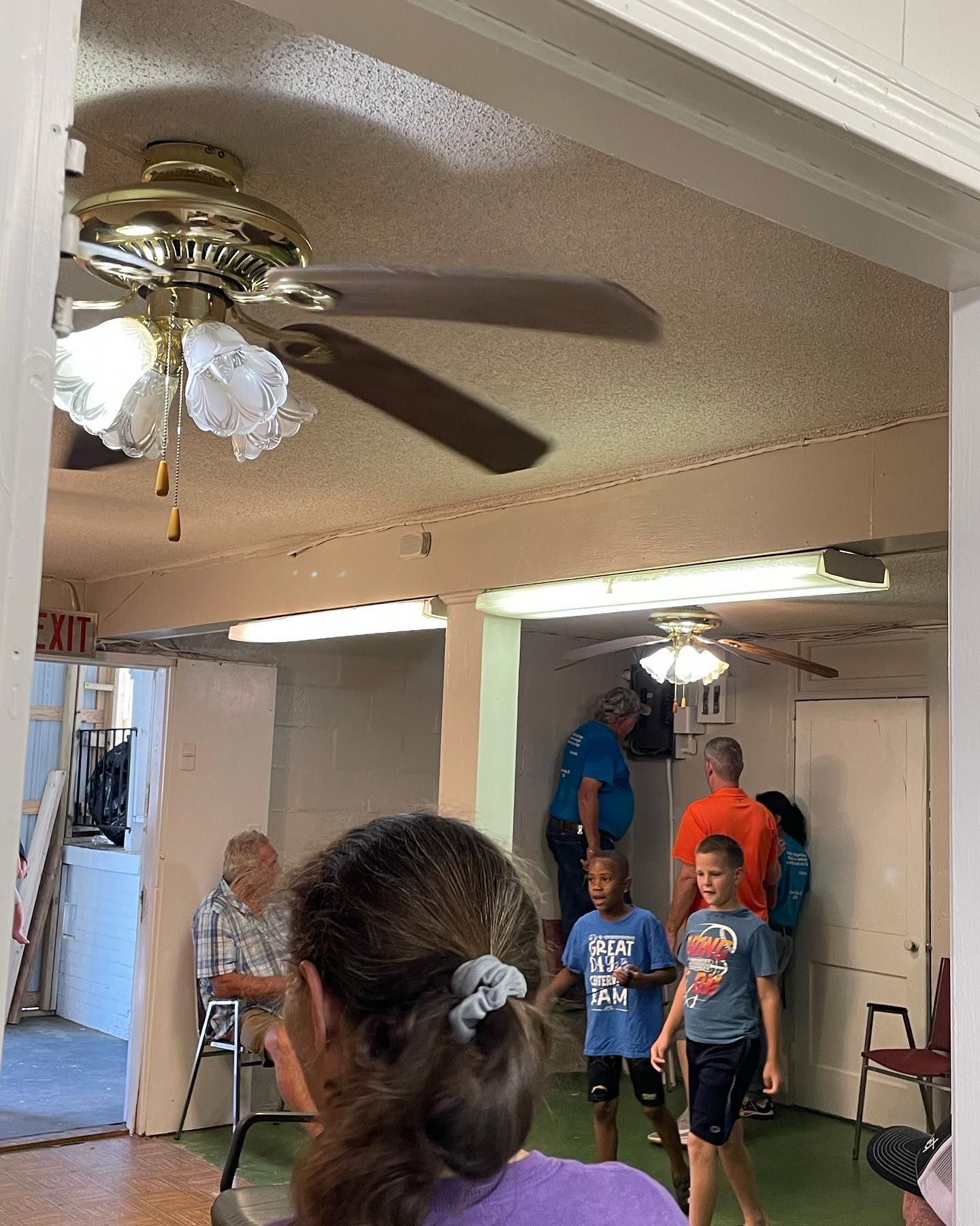 A group of people are standing in a room with a ceiling fan and a sign that says exit