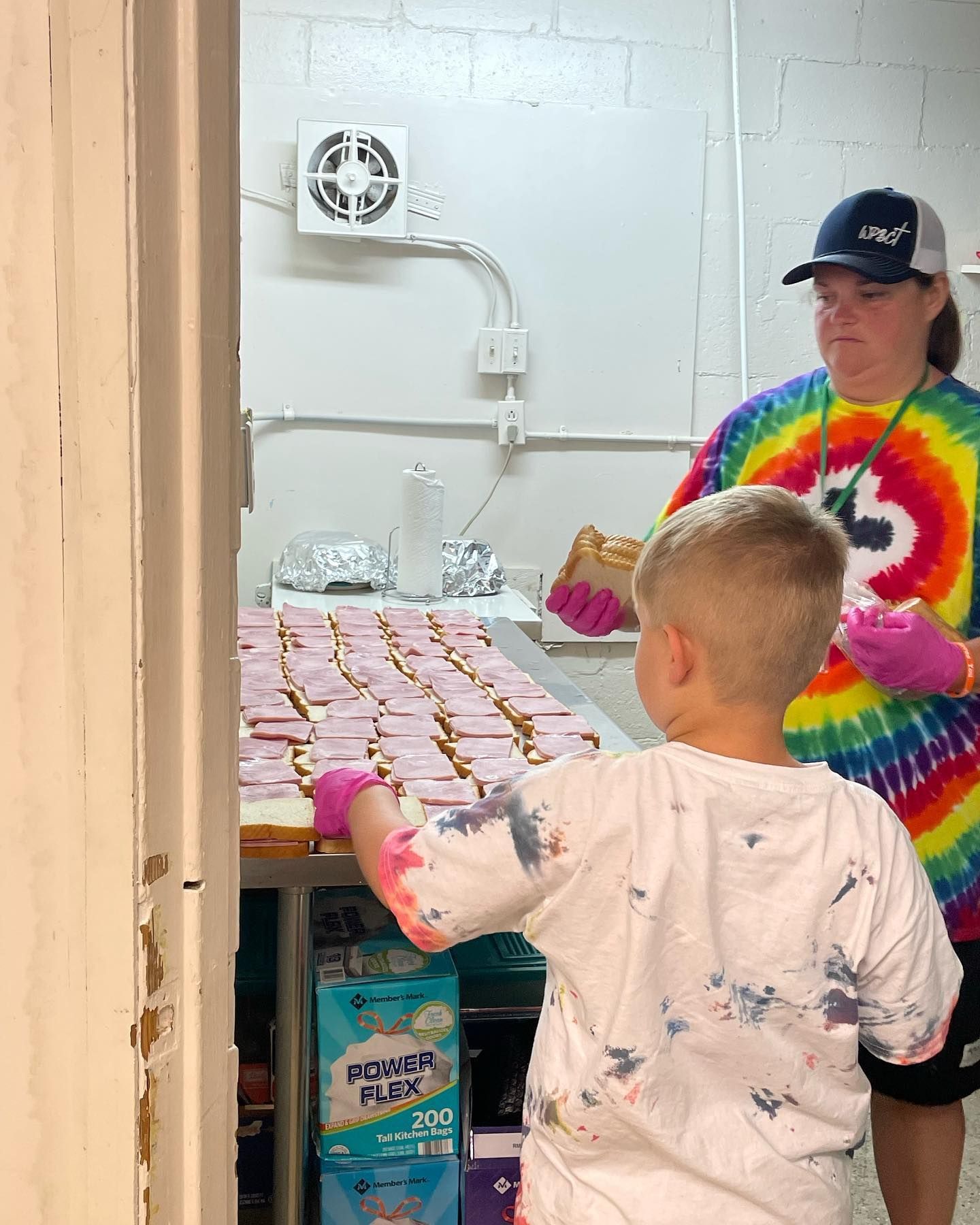 A woman in a tie dye shirt is standing next to a boy in a kitchen.