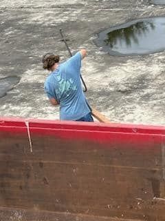 A man in a blue shirt is fishing in a red boat.