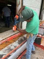A man in a green shirt and hat is working on a door.