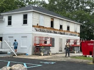 A man is standing in front of a white house being remodeled.