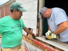Two men are working on a window on a building.