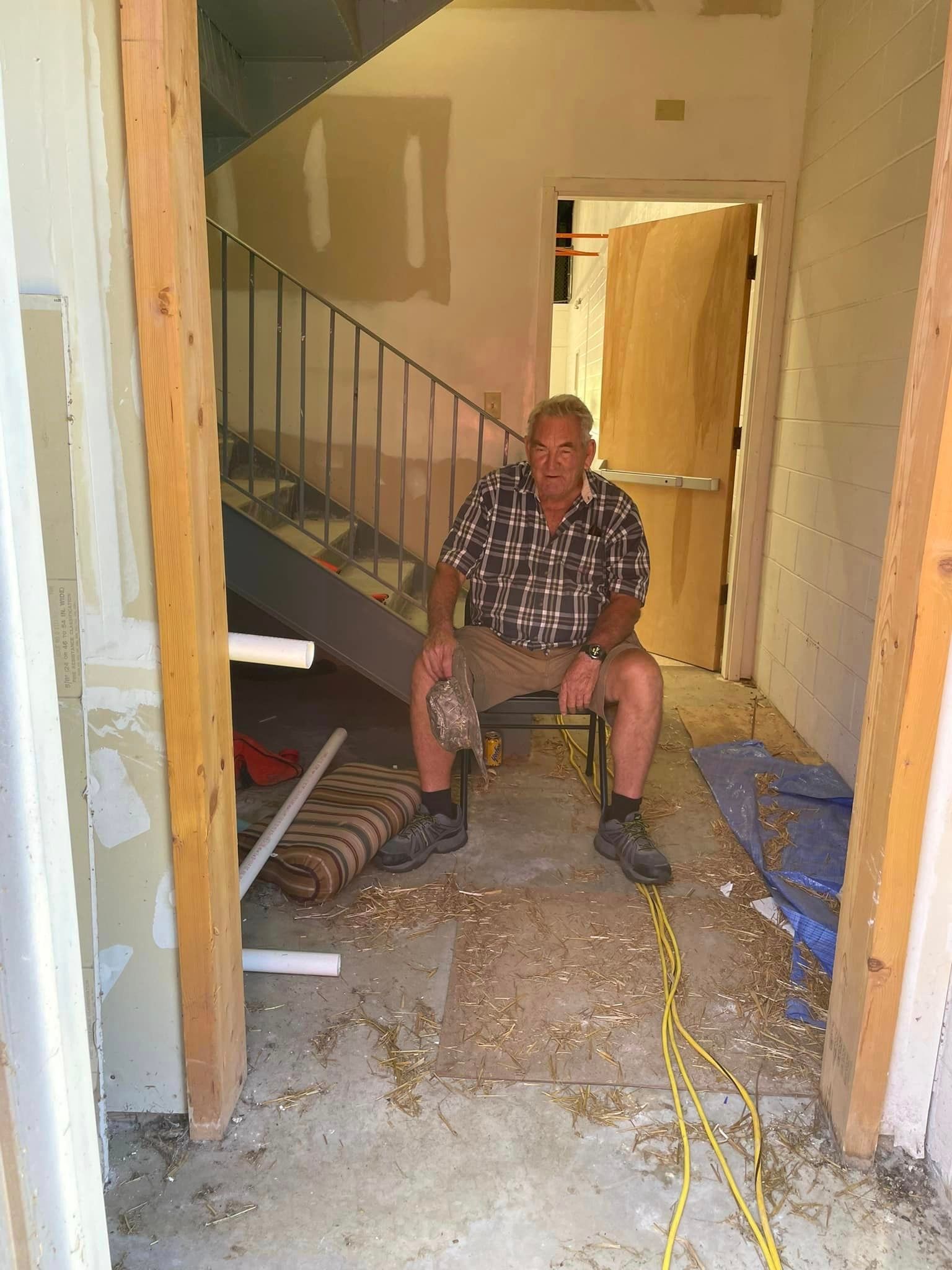 A man is sitting in a chair in a room next to a staircase.