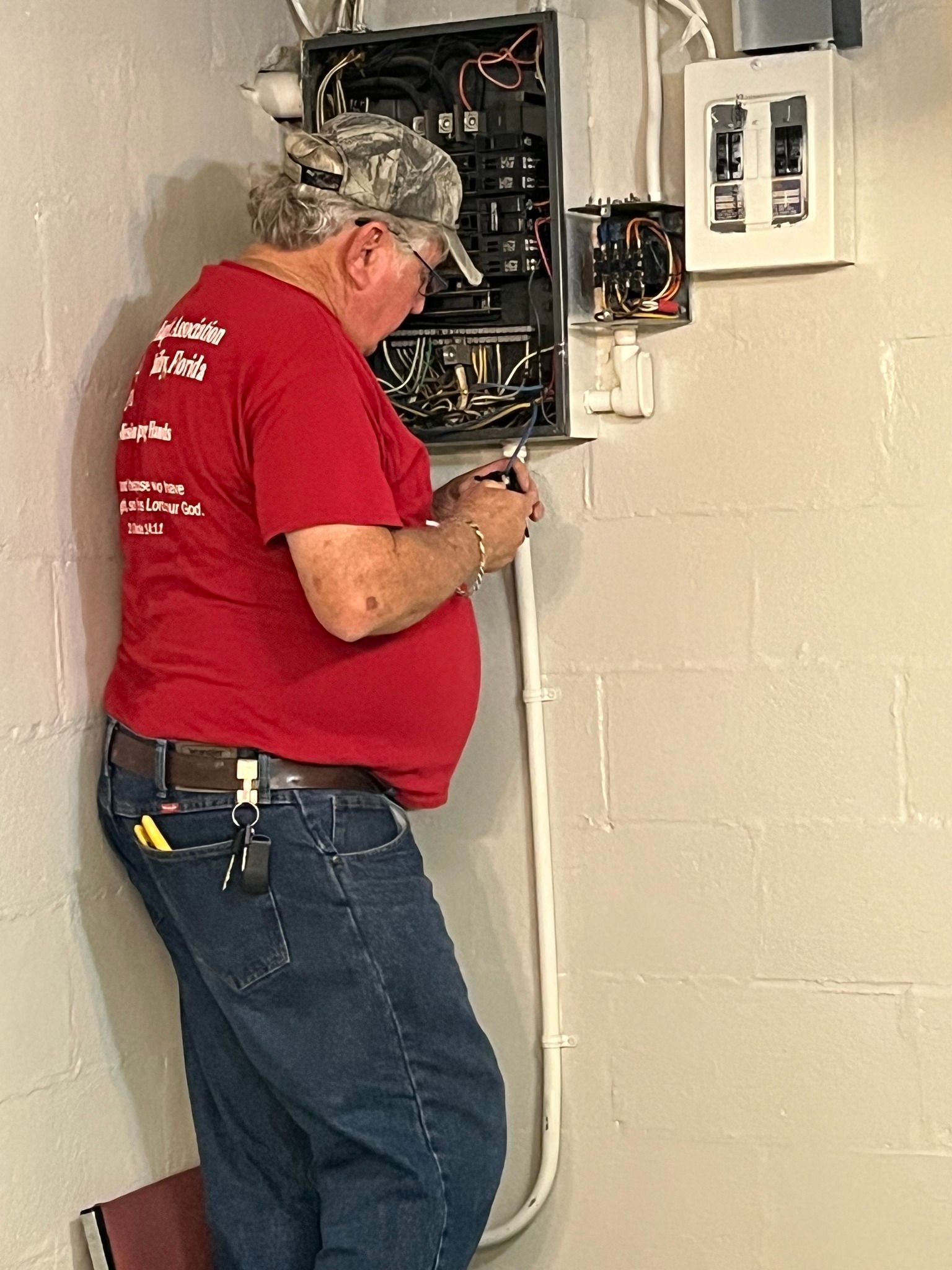A man in a red shirt is working on an electrical box.