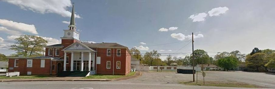 A church with a steeple is sitting on the side of the road.