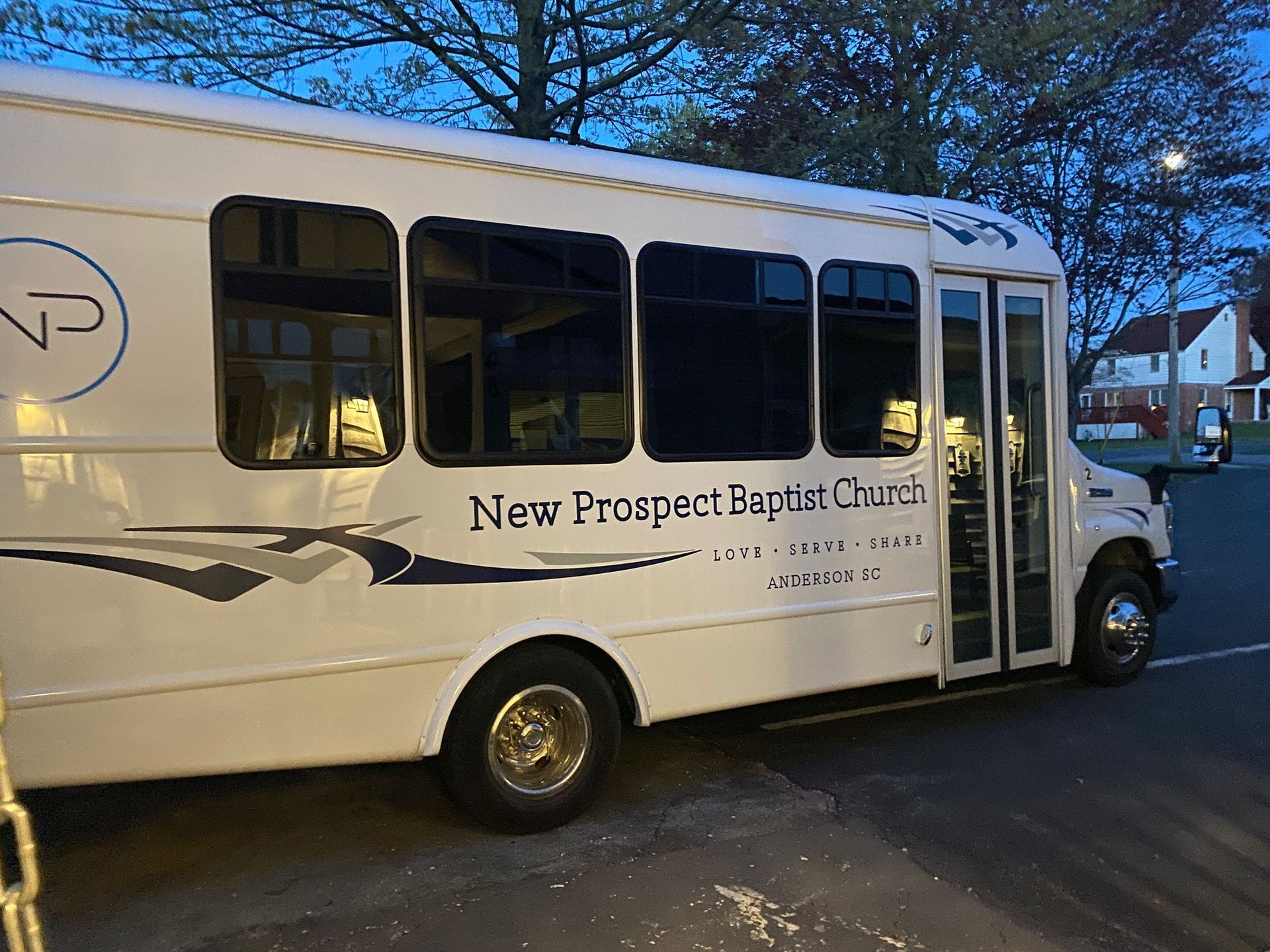 A white church bus is parked in a parking lot