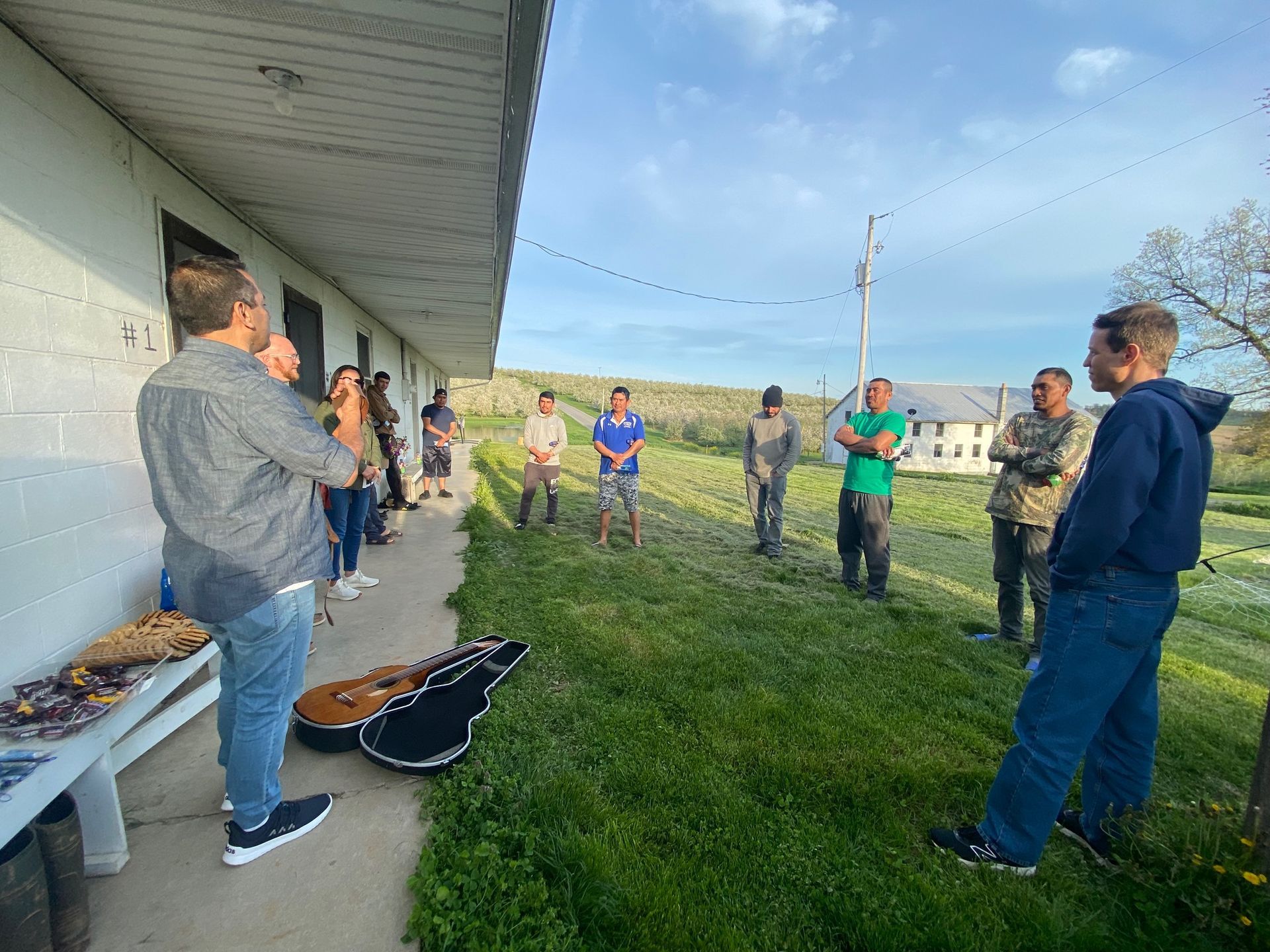 A group of people are standing outside of a building with a guitar in the grass.