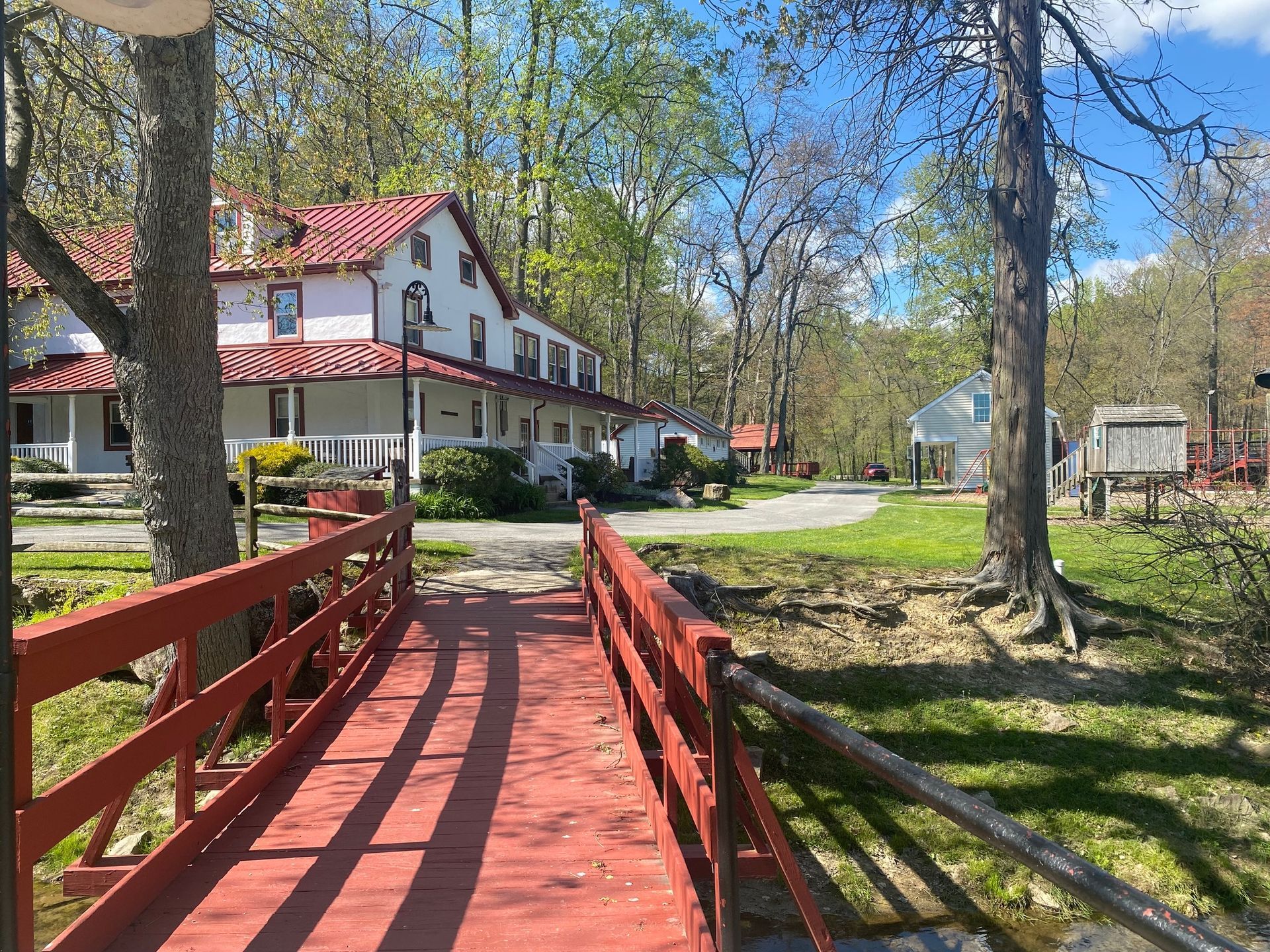 There is a red bridge leading to a house in the background.