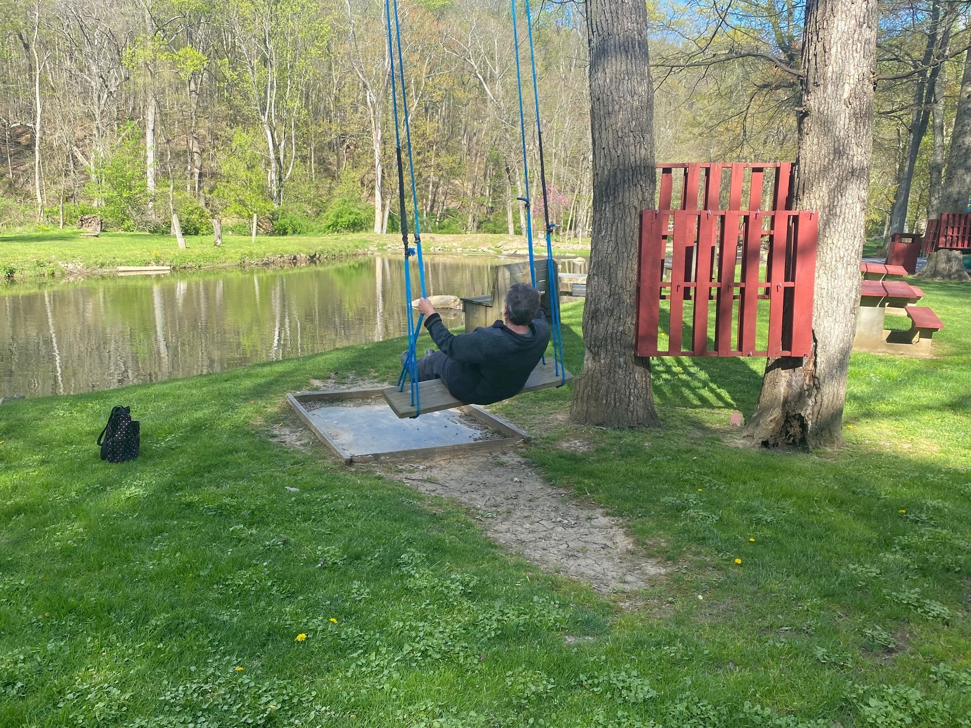 A man is sitting on a swing next to a lake.