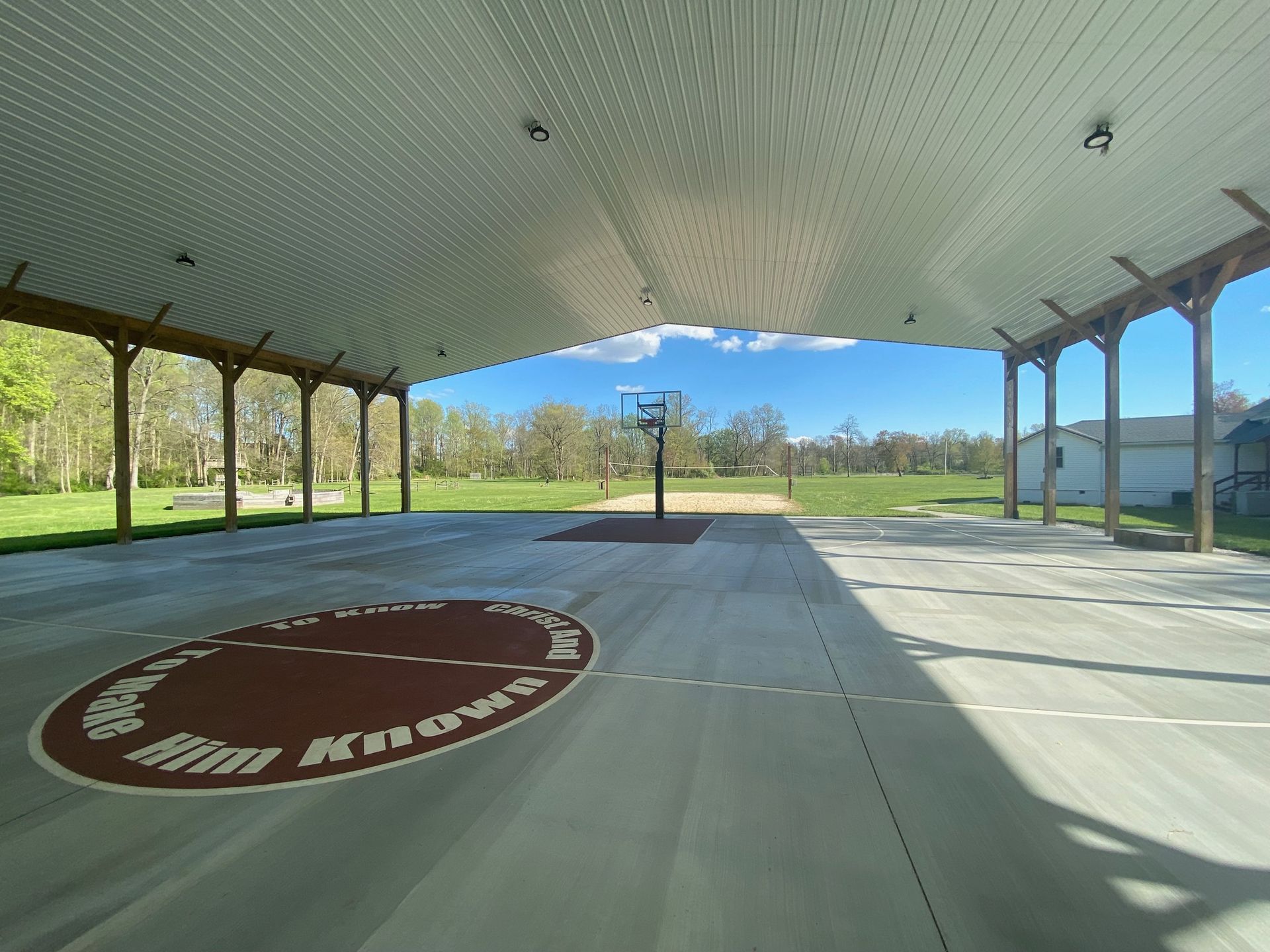 A basketball court under a canopy with a logo on the floor.