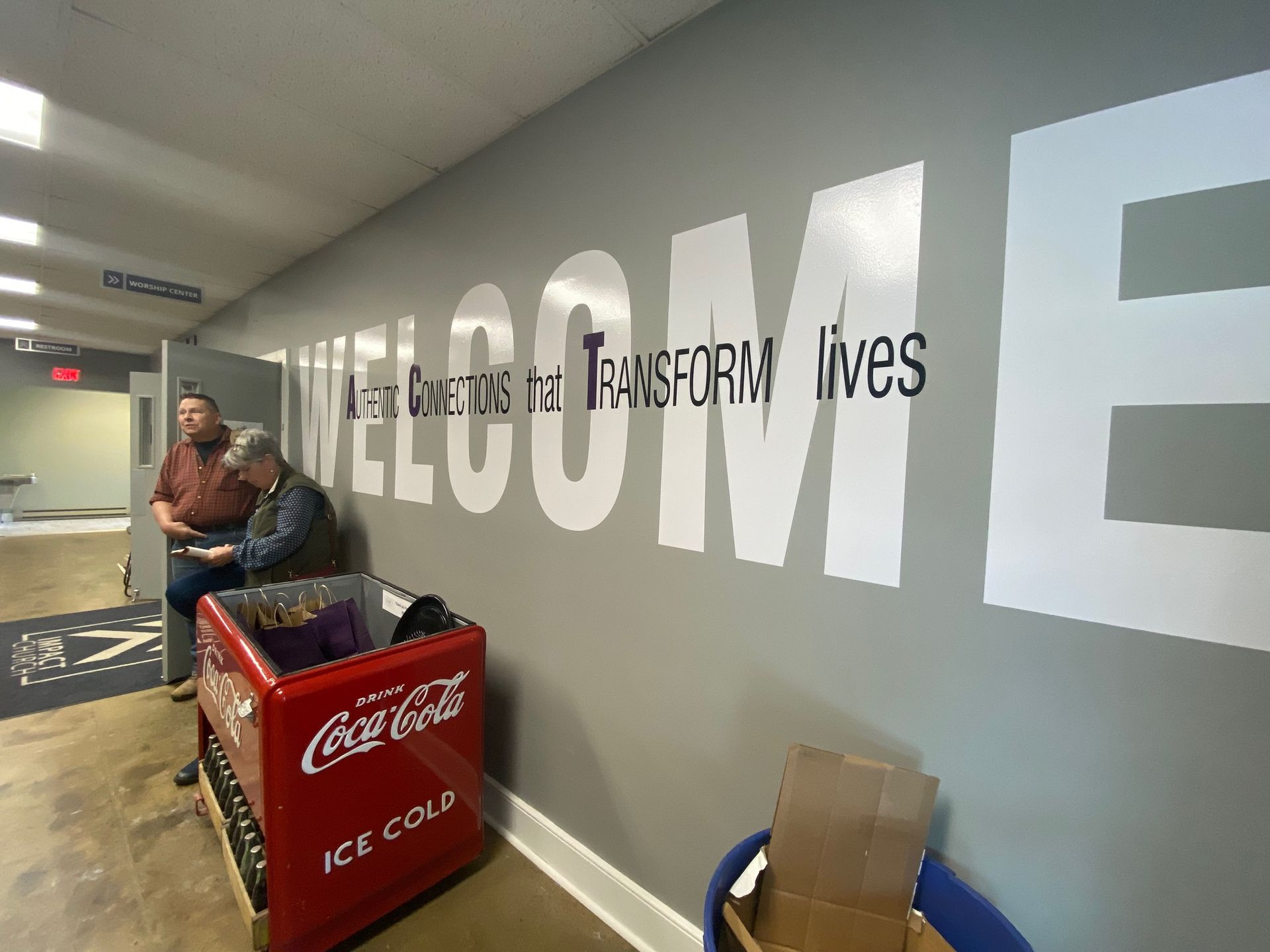 Two men are sitting in front of a wall that says welcome.