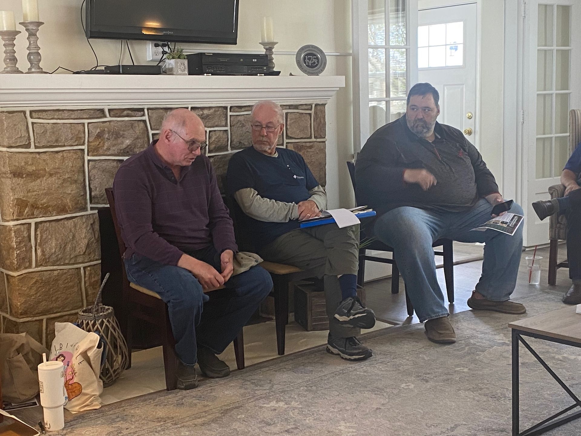 Three men are sitting in front of a fireplace in a living room.