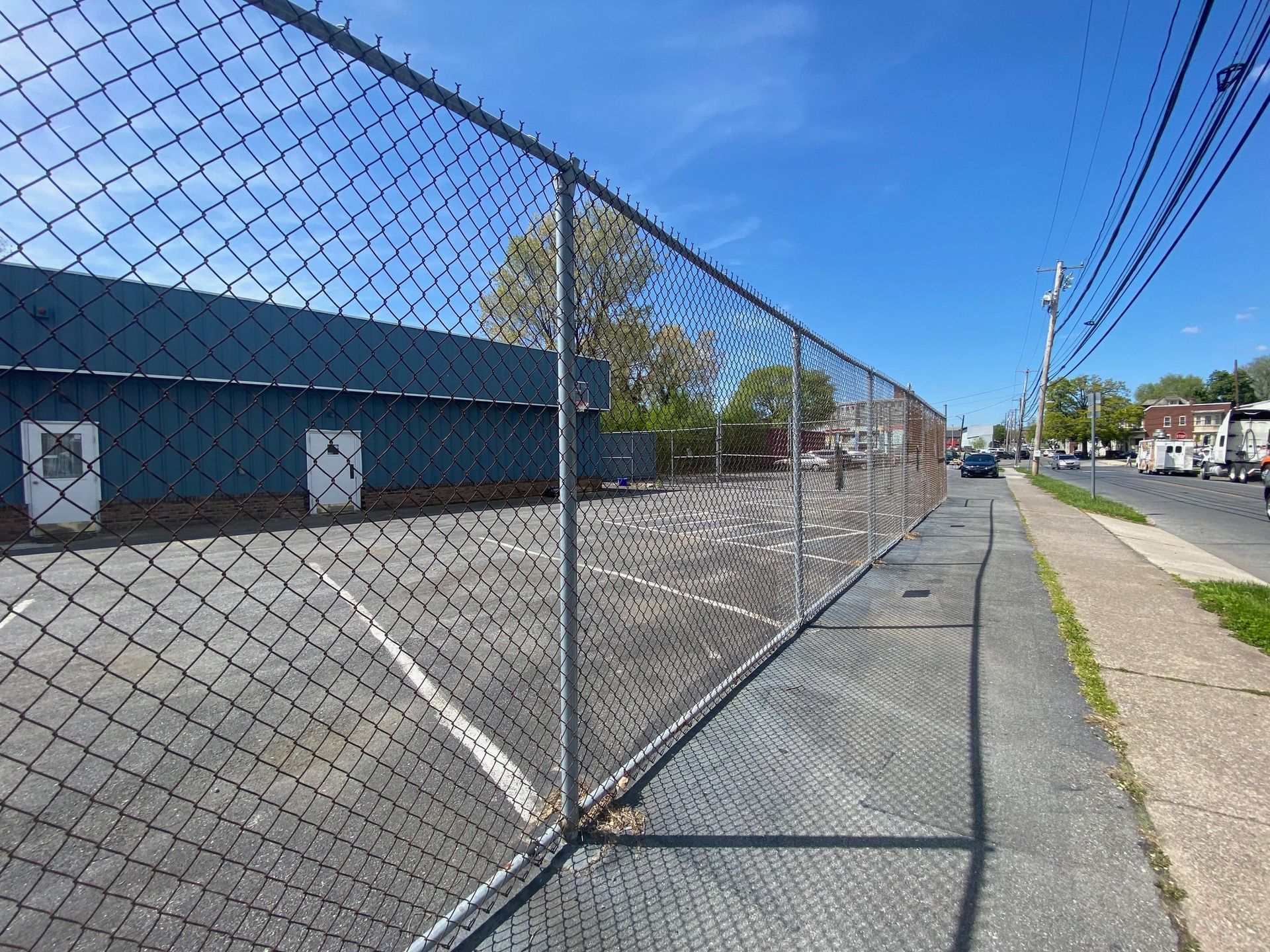 A chain link fence surrounds a parking lot with a building in the background.