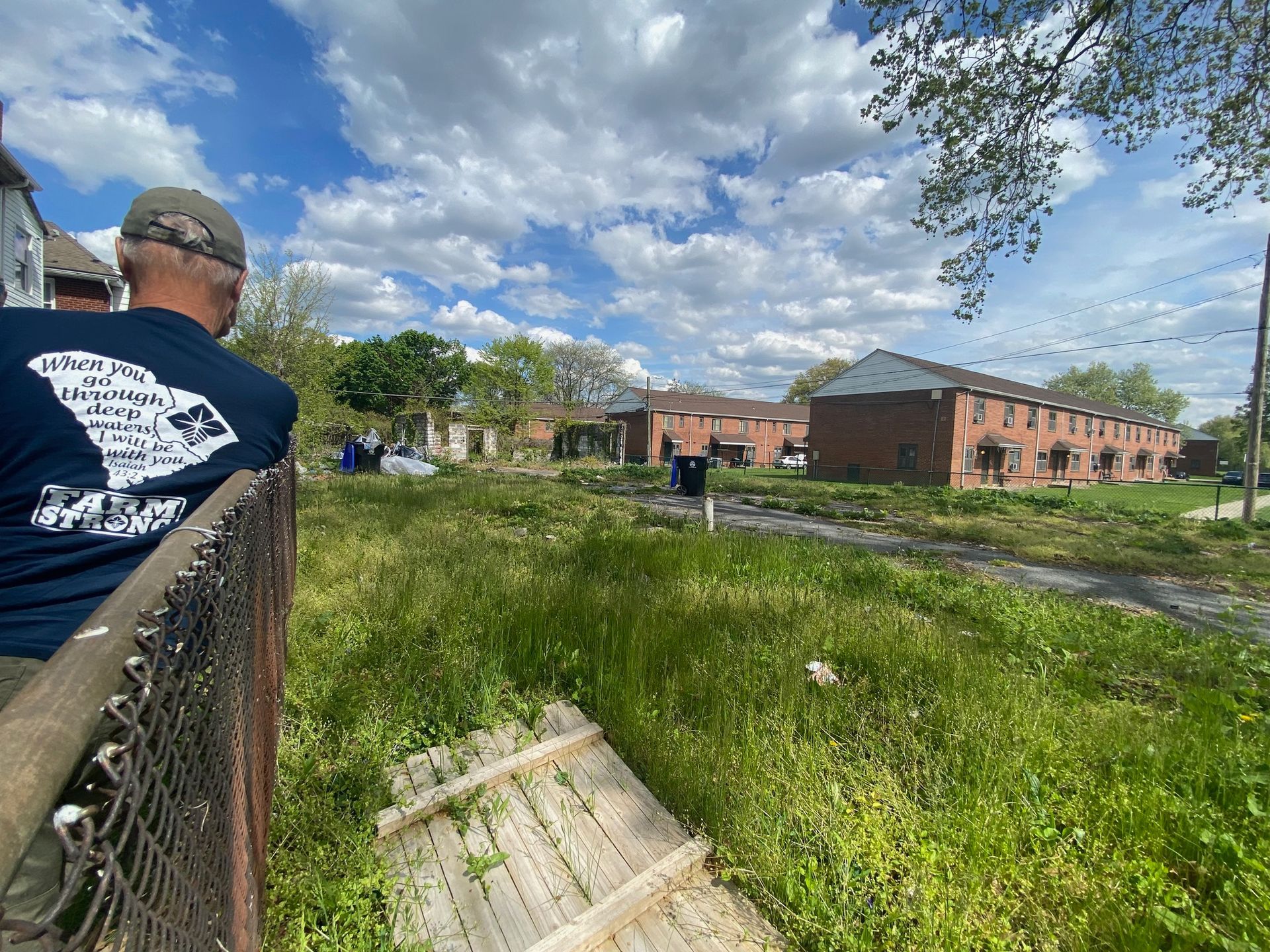 A man in a blue shirt is standing next to a chain link fence.