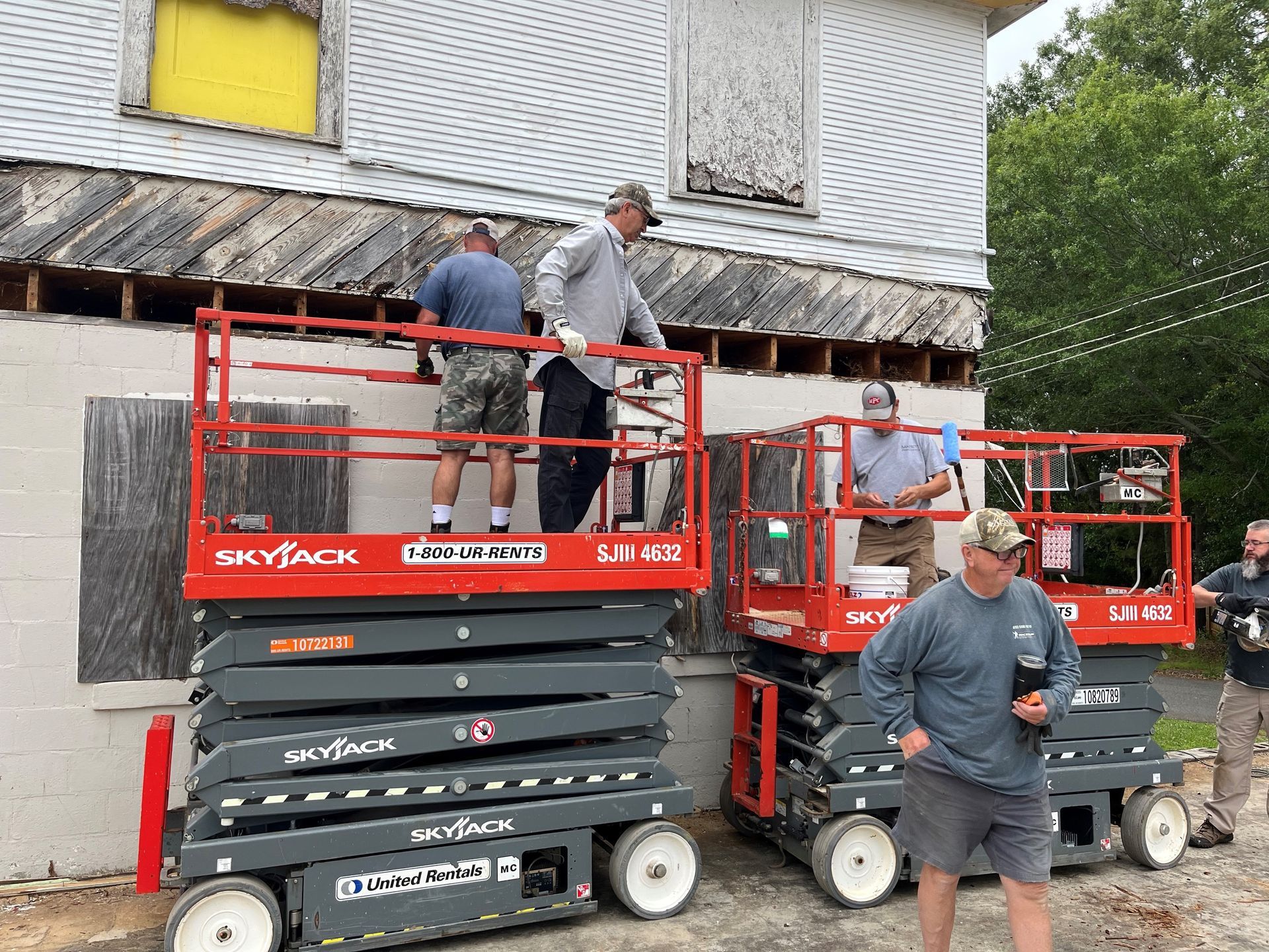 A group of men are standing on scissor lifts in front of a building.