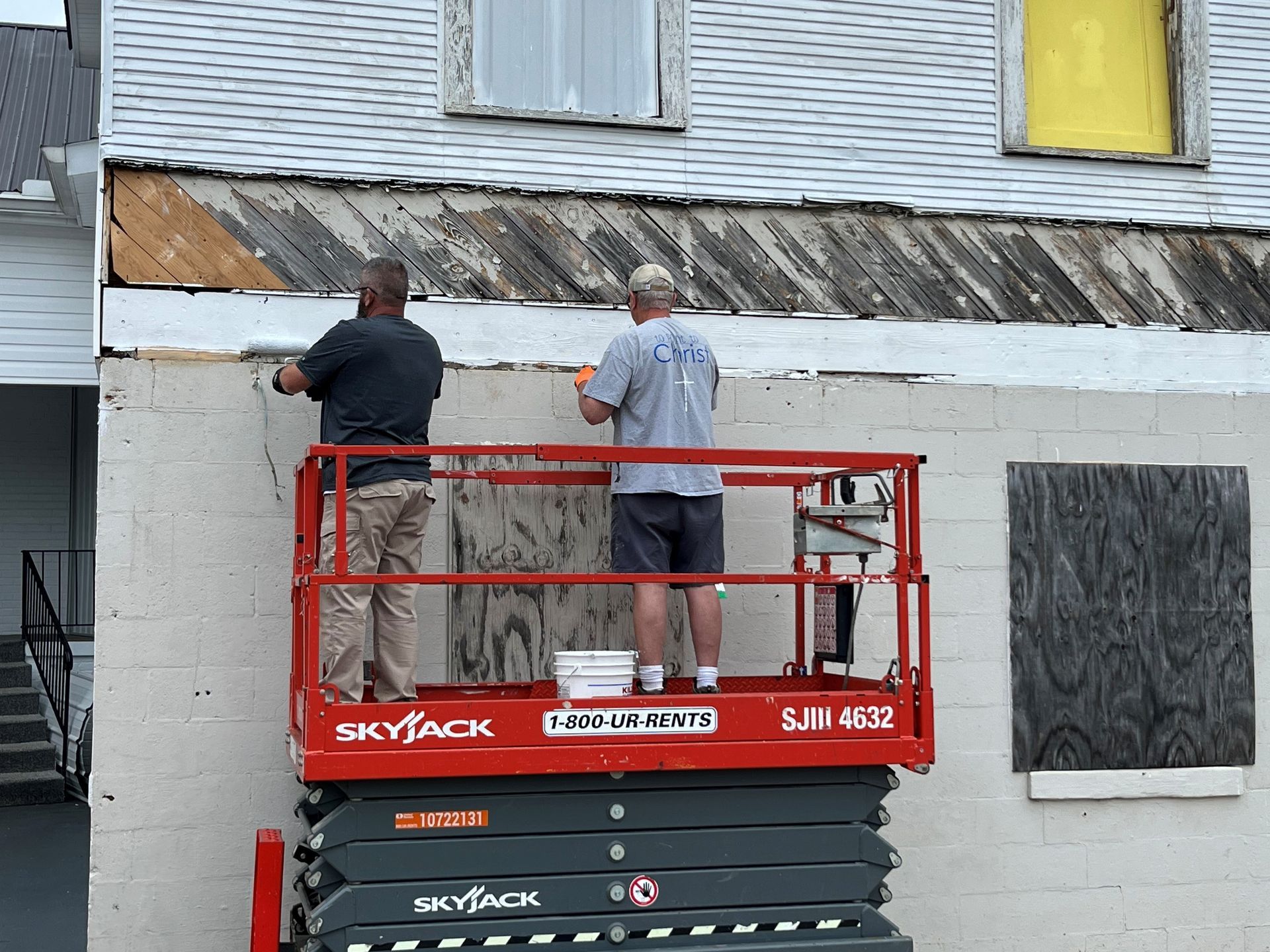 Two men are working on the side of a building on a skyjack lift.