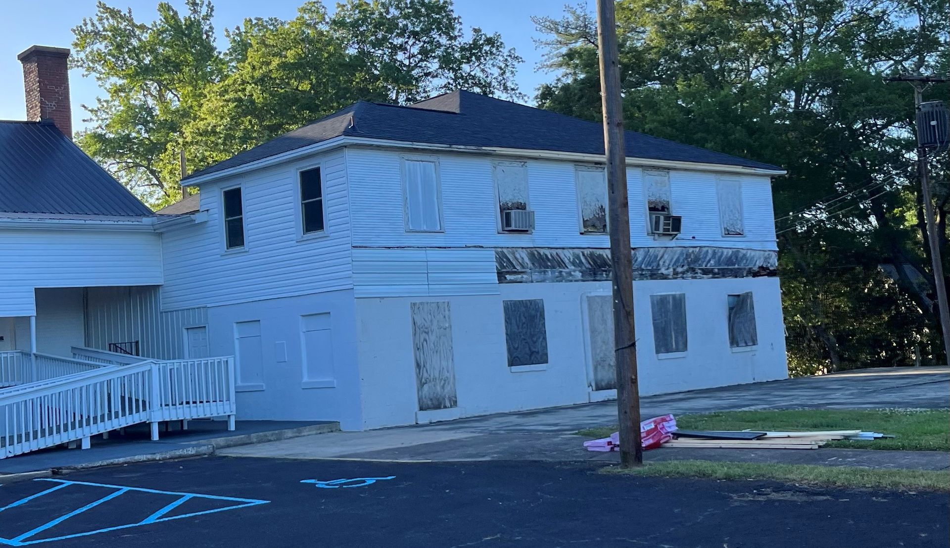 A white house with a black roof is sitting in the middle of a parking lot.