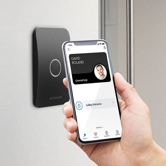 Hand holding a smartphone near a wall-mounted smart access reader displaying a digital ID card