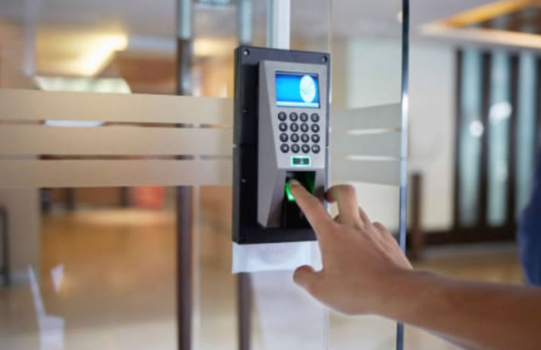 Hand pressing a keypad on a wall-mounted access control panel by a glass door