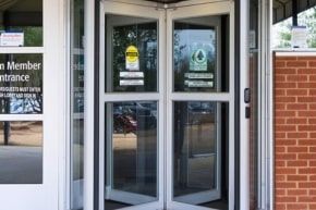 Glass double doors at a building entrance with a brick wall and entrance signage рядом