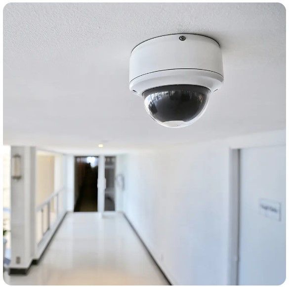 Ceiling-mounted security camera in a bright hallway corridor