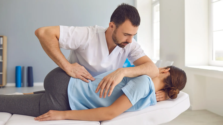 Chiropractor adjusting a patient's back on an examination table. White-coated man, hands on woman's back, in a light room.