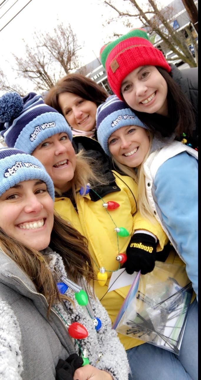 Five people smiling for a selfie, wearing winter hats. One holds string of Christmas lights.