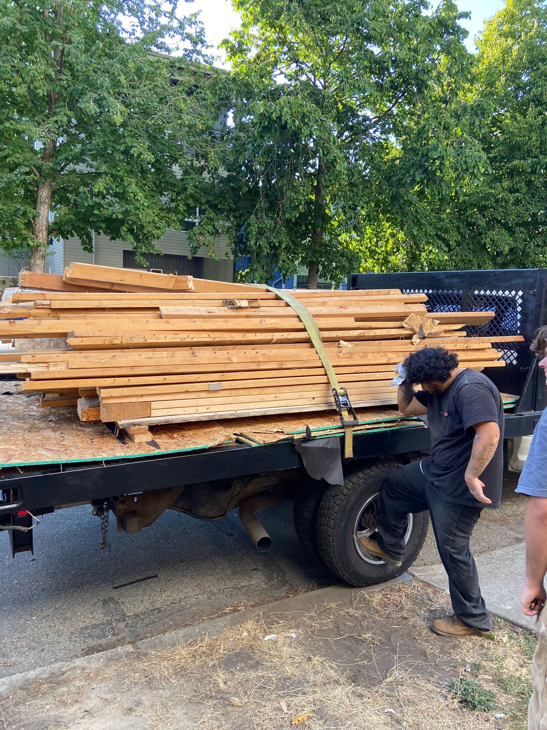 A man is standing next to a truck loaded with wood.