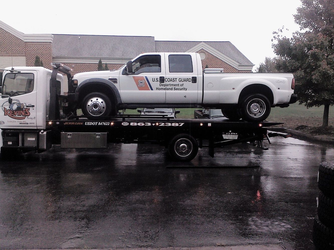White tow truck loading a white pickup truck in the rain
