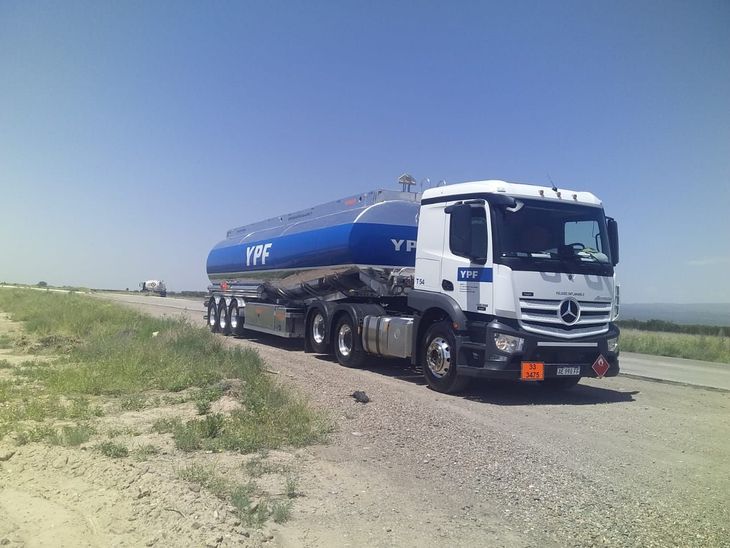 Un camión cisterna de combustible de YPF circula por un camino de tierra bajo un cielo azul.