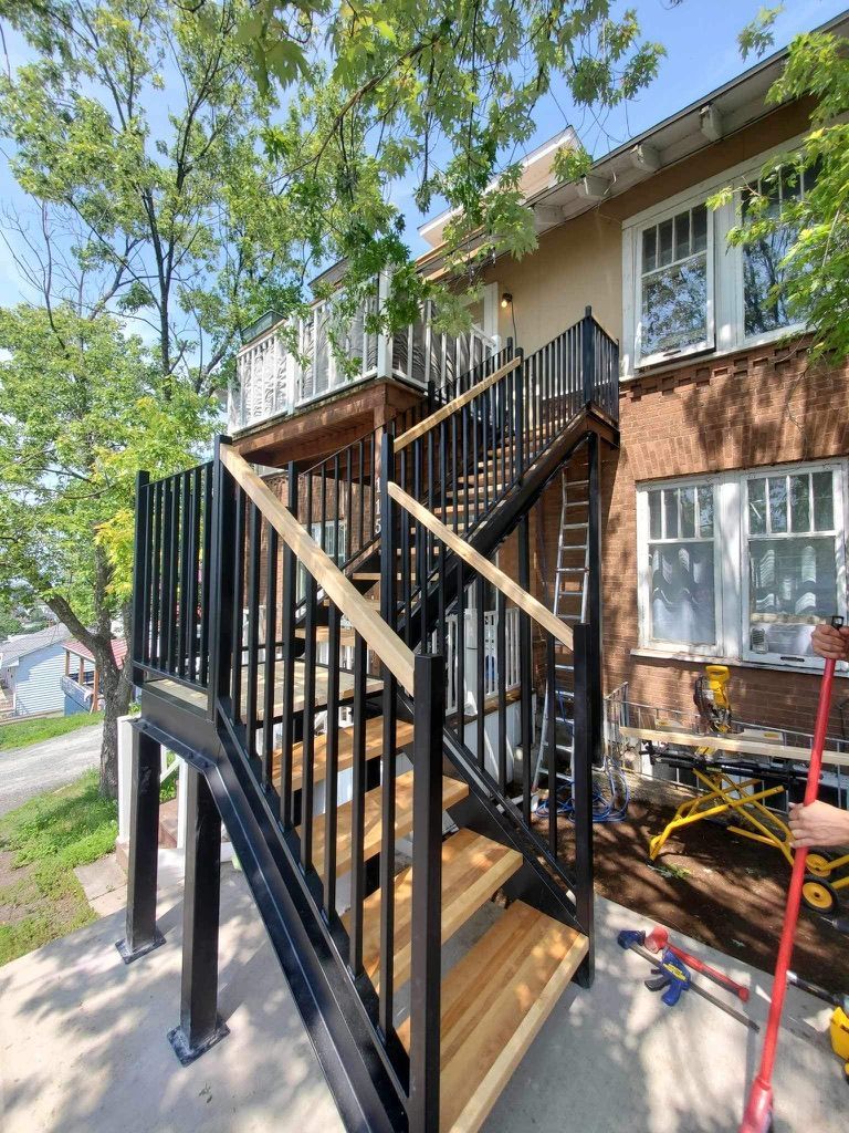 Une personne tient une serpillière devant une maison avec des escaliers.