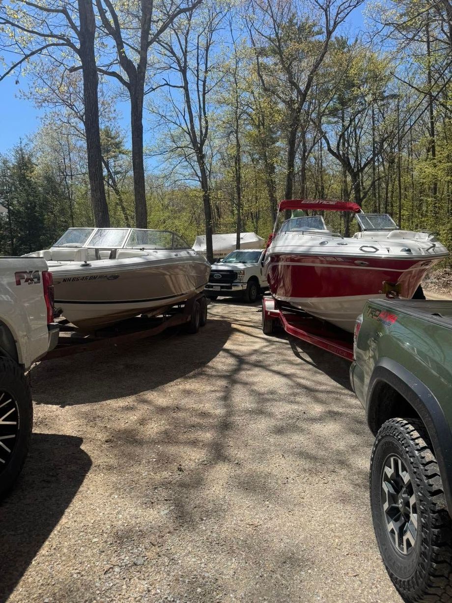 Two boats parked on a gravel driveway, one silver and one red, with a truck at the edge of frame.