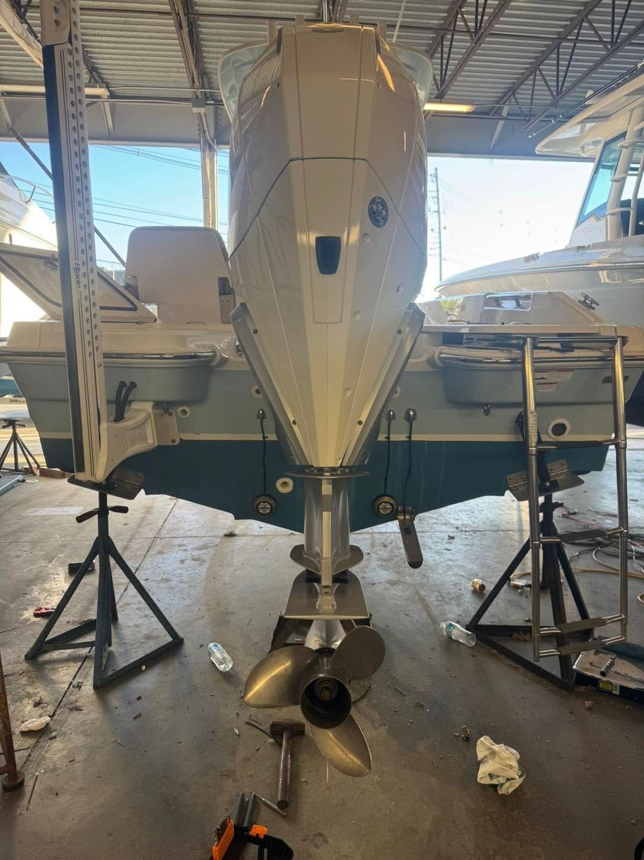 Front view of a white boat on stands inside a workshop, with a propeller and jack stands visible.