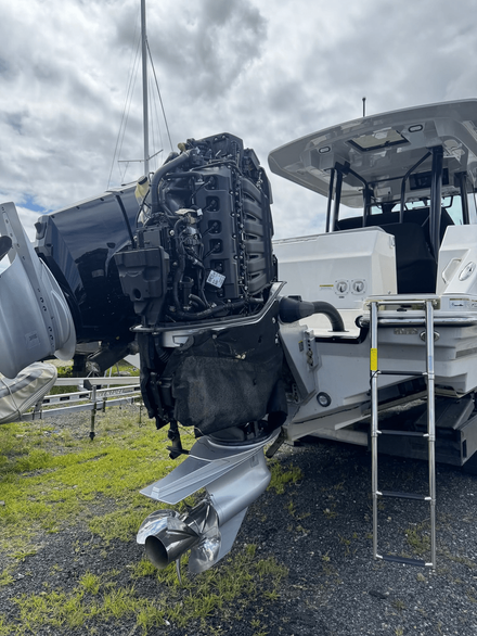 Damaged boat motor hanging beside a white boat on a trailer in a gravel lot