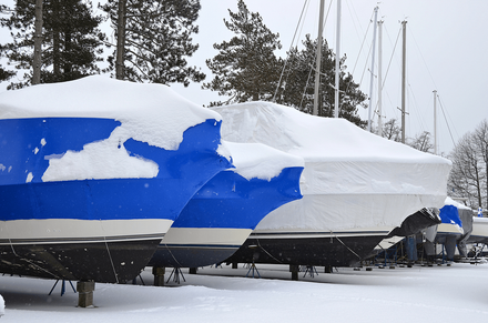 Snow-covered sailboats in a marina, wrapped in blue and white covers.