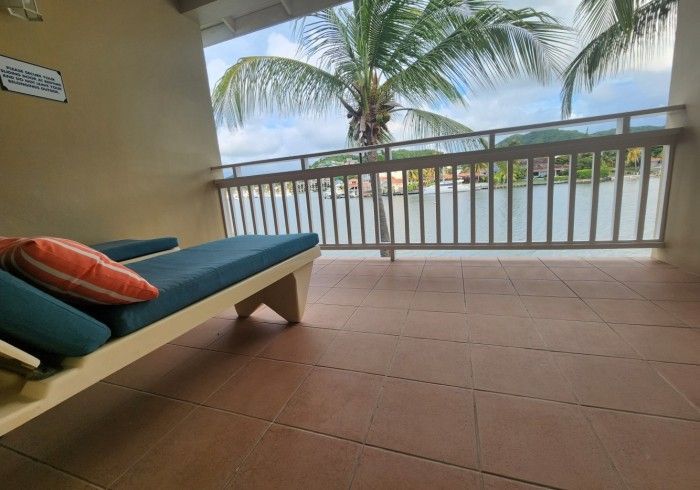 Covered patio with a blue lounge chair, orange pillows, and a view of palm trees and water